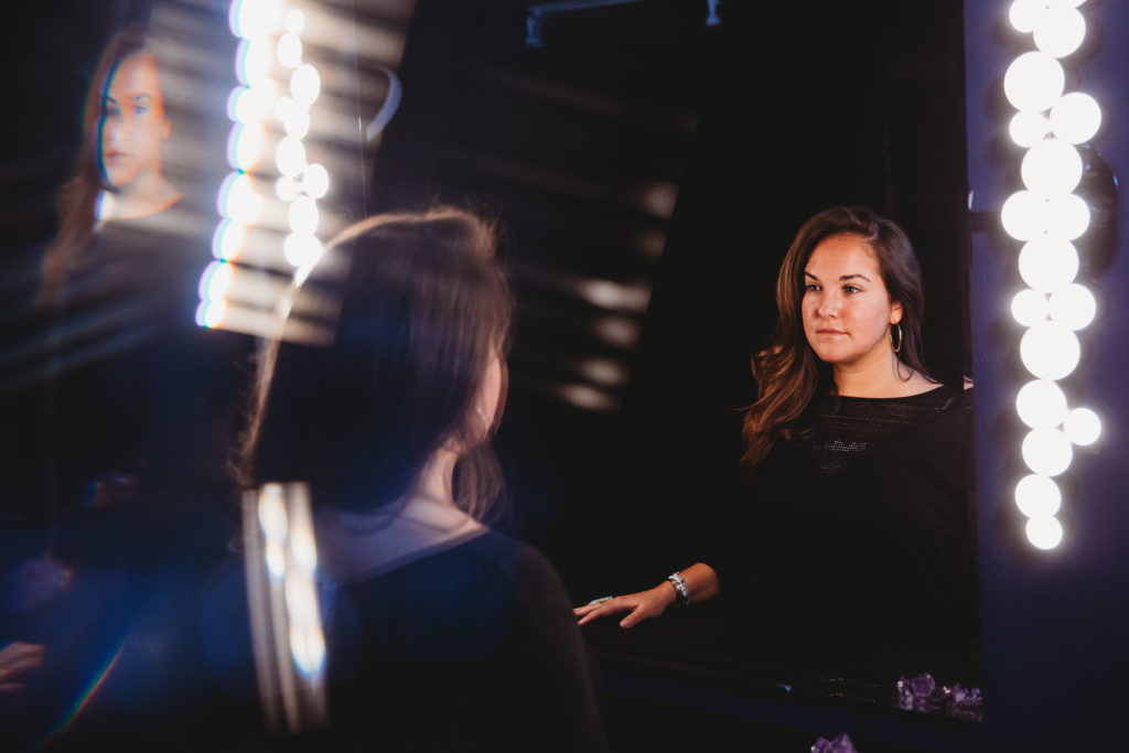 Woman in black looking at herself in the mirror with a dark background.  Learning to Live an Embodied Life.  Photography by Lindsay Hite
