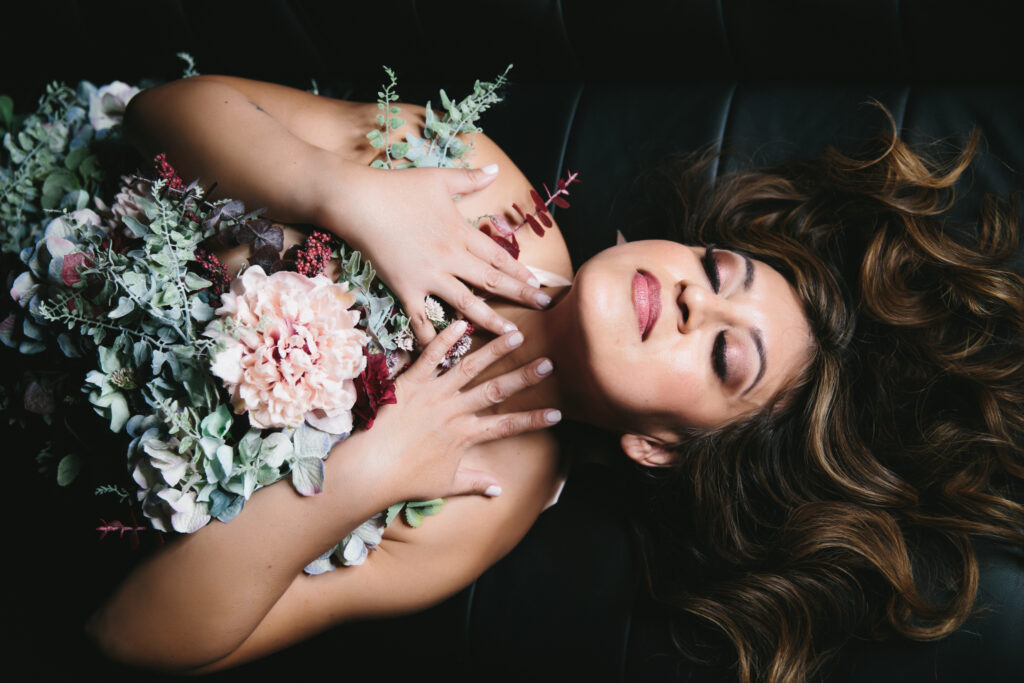 Woman over 40 with a bouquet of flowers on her chest with a dark backdrop.  Photography by Lindsay Hite. 