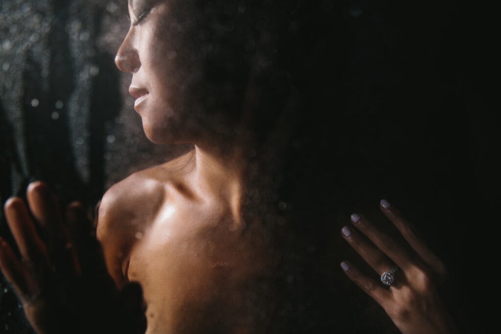 Asian woman pictured upper chest and above in a shower with a black background.  Boudoir photography by Lindsay Hite.