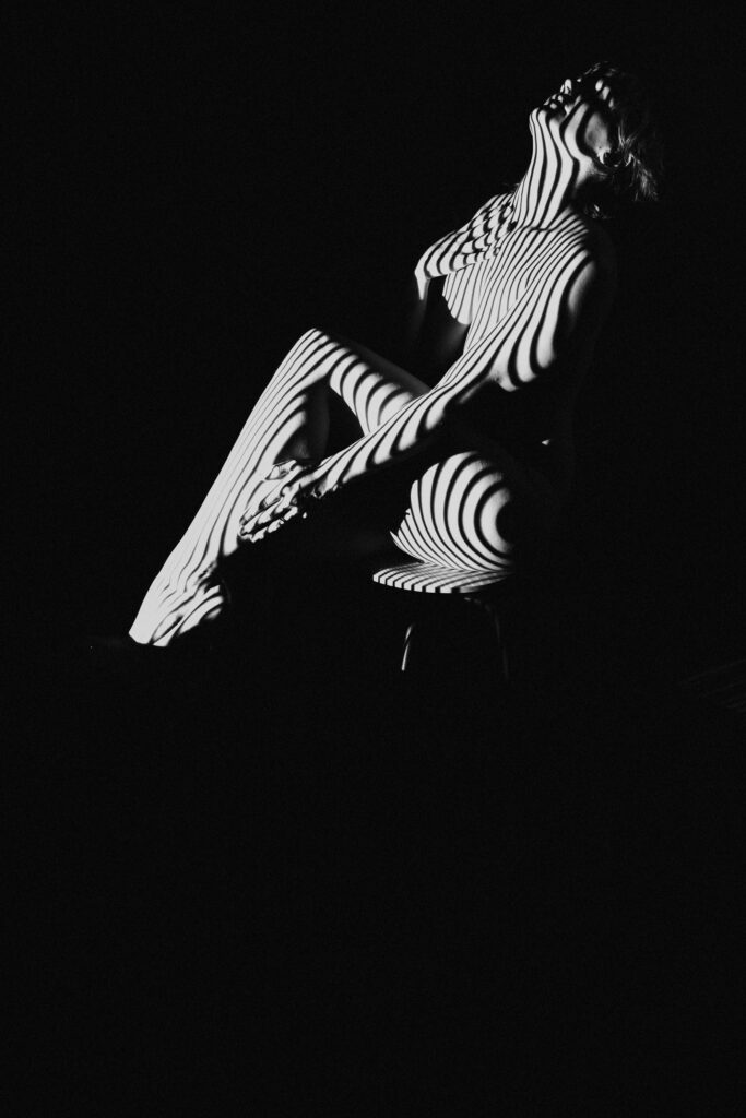 Image of a naked woman's backside with stripes superimposed over her with a dark background.  She talks about how getting nearly naked her her self-confidence  Photography by Michelle DeVoe at Show Your Spark