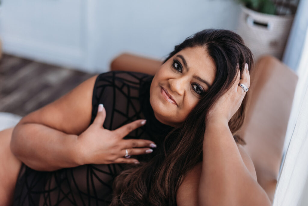 Woman in black lace leotard sitting on a leather sofa. Photography by Lindsay Hite.