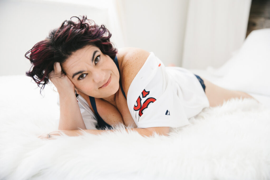 Woman in red socks jersey and navy bra set laying on her belly on a white fur-lined bed. Photography by Lindsay Hite