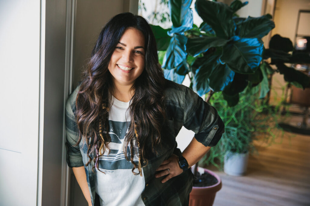 Casual headshot of a woman with brown wavy hair wearing a t-shirt and flannel button down shirt. Photography by Lindsay Hite.
