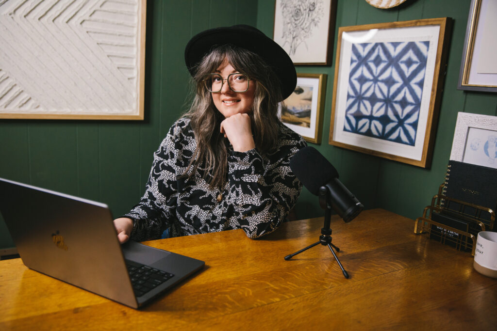 Woman wearing a black hat, sitting at her computer and podcasting microphone. Branding photography by Lindsay Hite.
