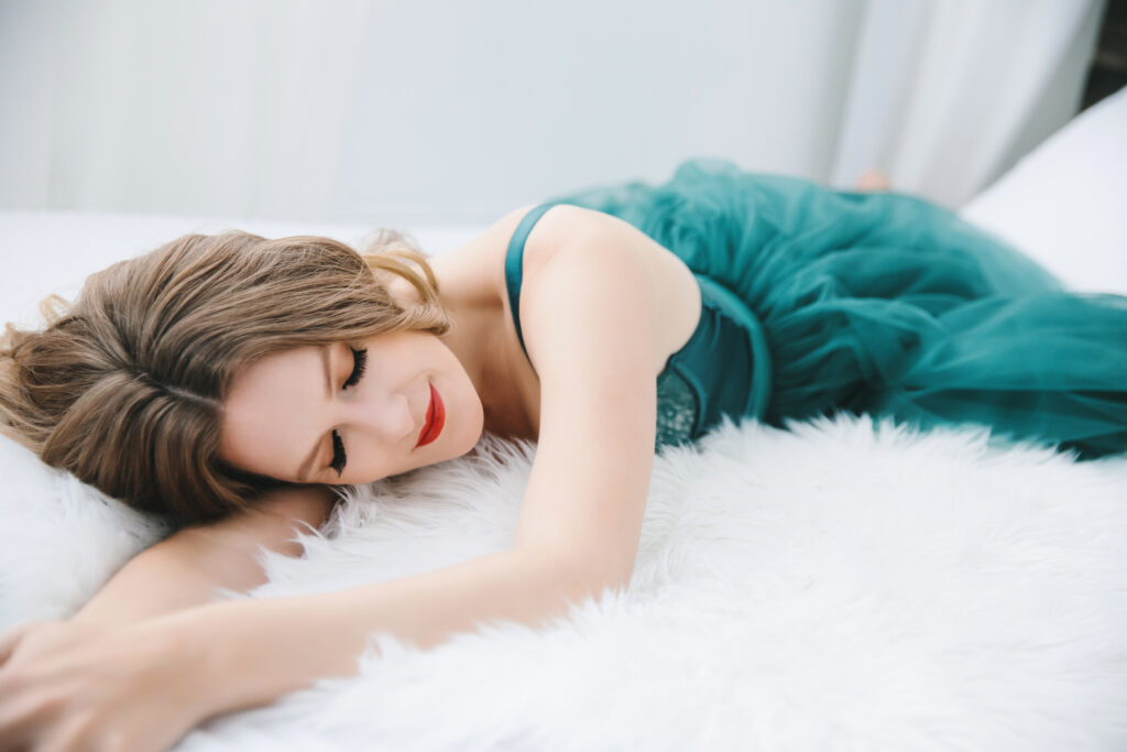 Woman in green toile dress laying on her belly on a fur-lined bed.  Photography Lindsay Hite