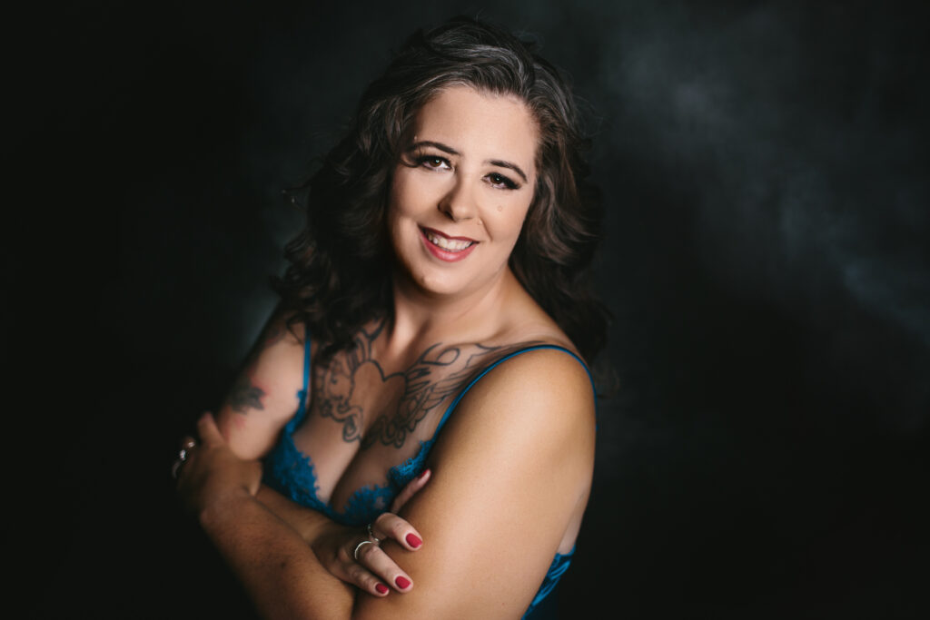 Woman in blue lingerie standing in a power pose against a black backdrop showing off her inner fierceness. Photography by Lindsay Hite