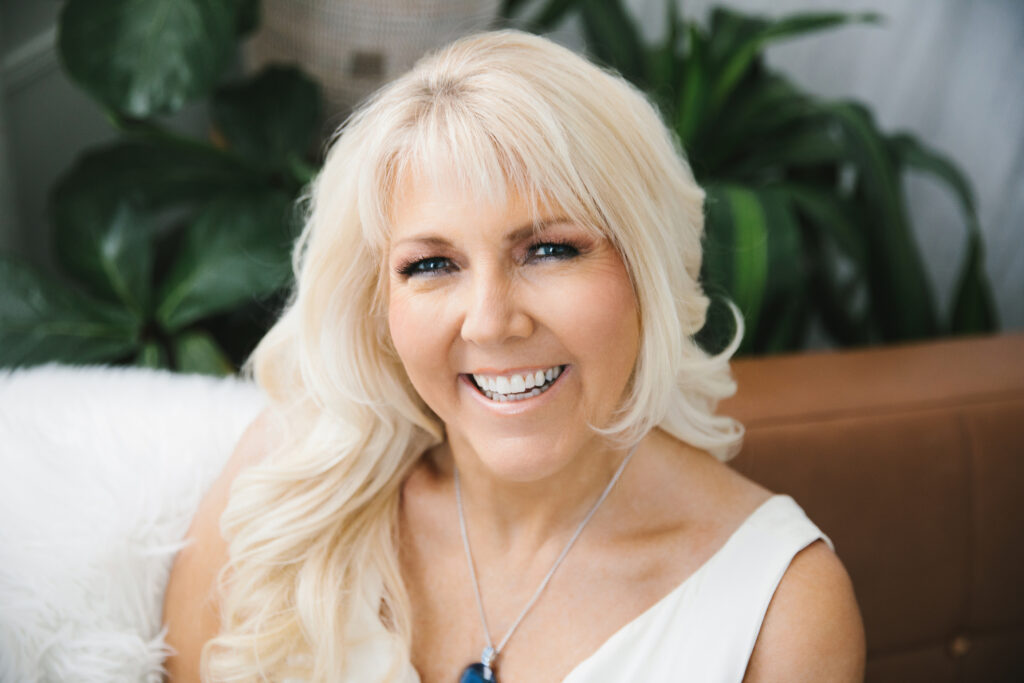 Women in white top sits on a tan sofa with plants in the backdrop.  Photography by Lindsay Hite