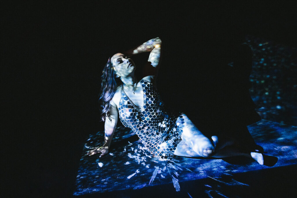 Woman in sequence top sitting on the floor with a black backdrop.  The Client told us she was 