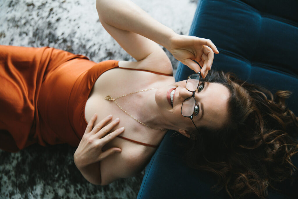 Woman in a burnt umber slip dress sitting on the floor leaning back on a navy blue sofa leaning back against the sofa. Photography by Lindsay Hite.