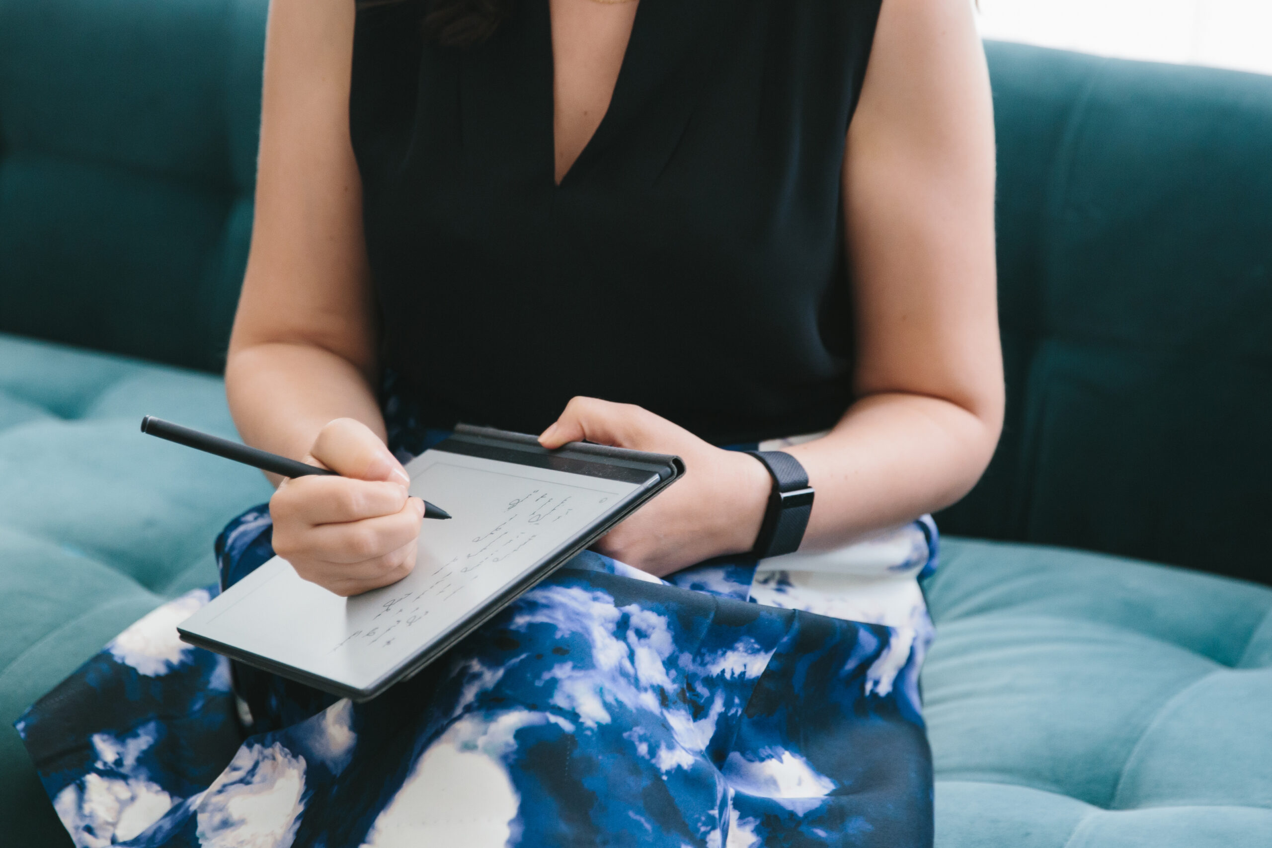 Portrait of a woman's torso sitting on a teal sofa writing in a notebook. Photography by Lindsay Hite.