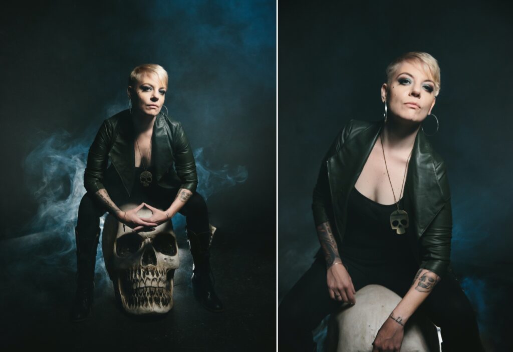 Woman in leather pants and jacket sitting on a large skull with a smokey backdrop. Photography by Lindsay Hite