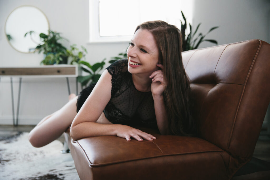Woman in black lingerie laying on her belly on a tan sofa happy after discovering her why. Photography Lindsay Hite