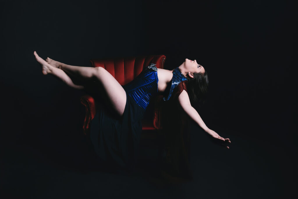 Woman in blue corset leaning back in a red leather chair. Photography by Lindsay Hite