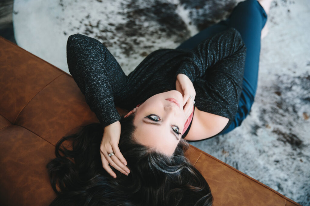 Woman in black sweater sitting on the floor leaning back against a leather sofa. Photography by Lindsay Hite