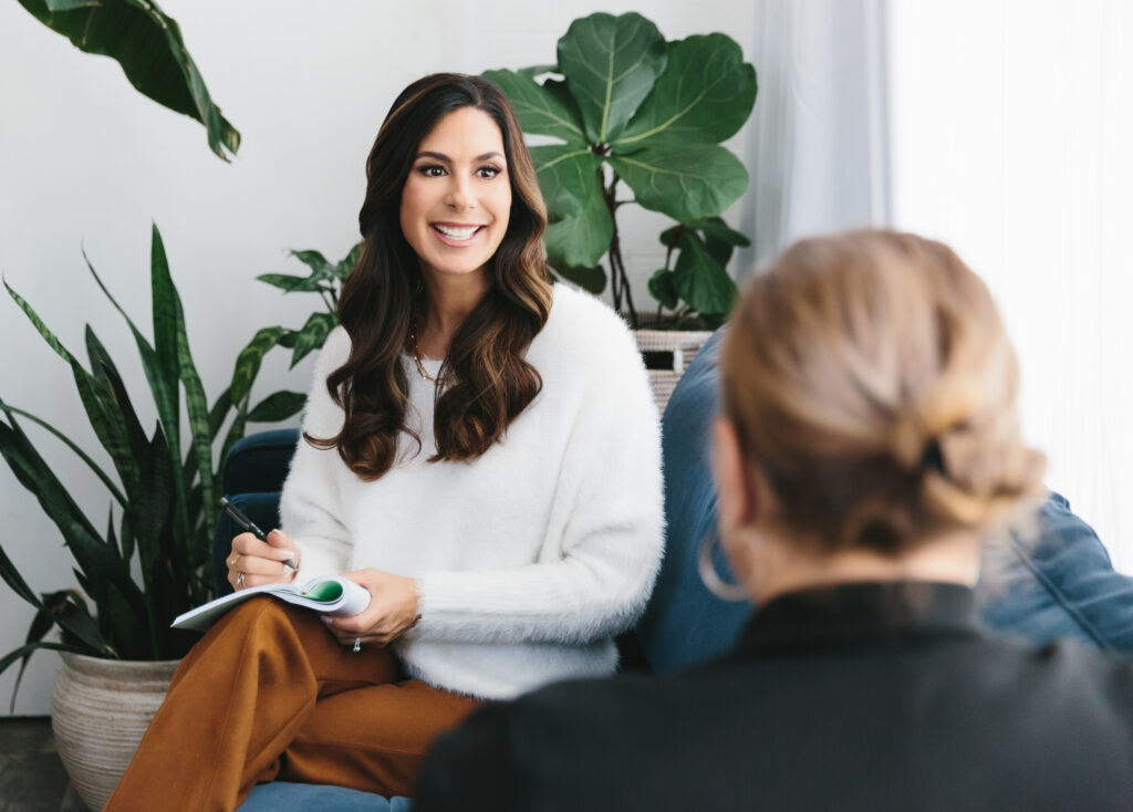 Woman smiling while leading a therapy session. She's wearing a white fuzzy sweater and tan pants. Photography by Lindsay Hite.