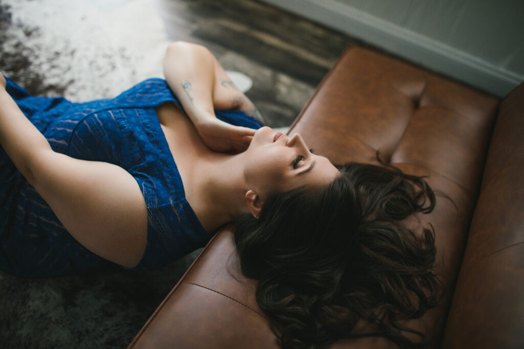 Woman in blue sundress leaning back against a tan leather sofa. Photography by Lindsay Hite