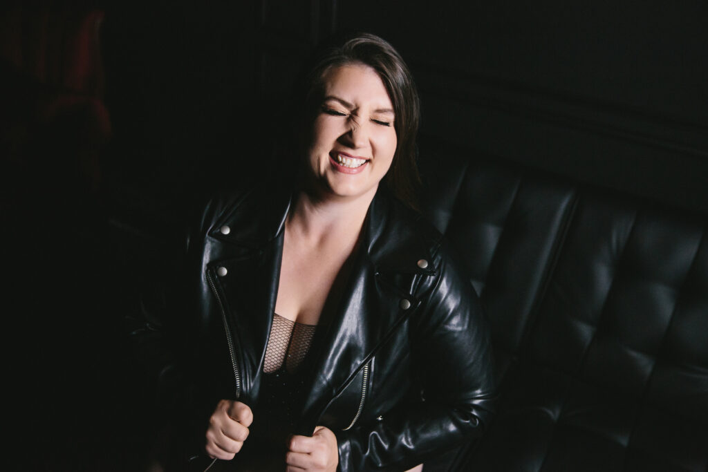 Woman in black jacket with black backdrop smiles bit showcasing her confidence as a fierce after forty woman. Photography by Lindsay Hite