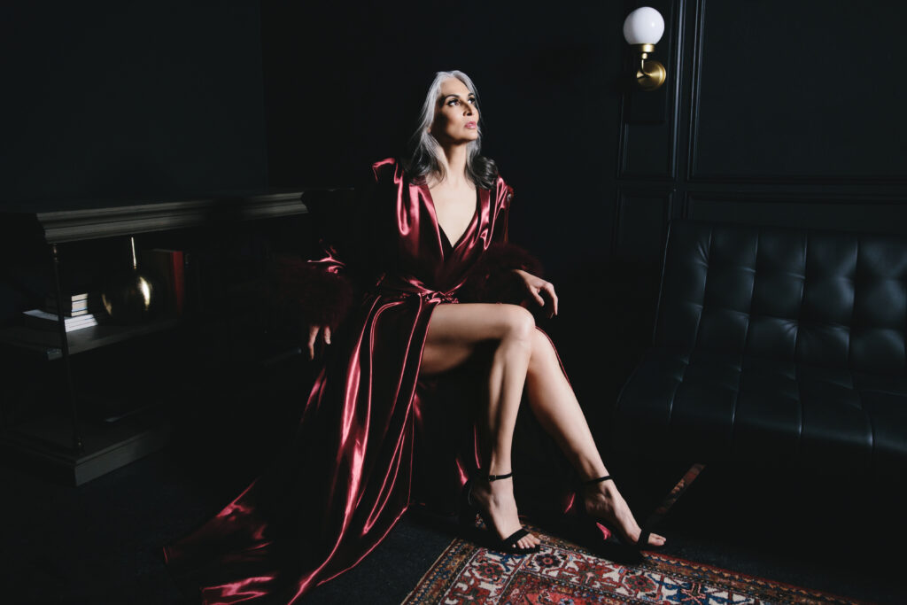 Woman in long dark blush silk robe in a black living room scene looking away from the camera. Photography by Lindsay Hite.