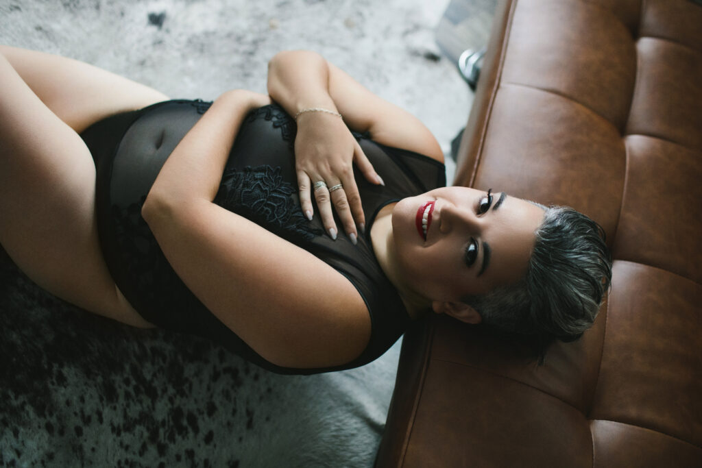 Woman in see through lingerie leaning back against a tan sofa looking directly at the camera. Photography by Lindsay Hite
