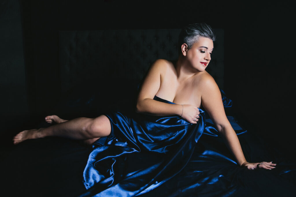 Woman in sapphire colored sheets with a dark backdrop. Photography by Lindsay Hite