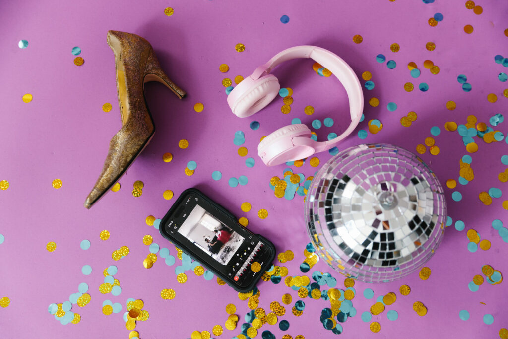 Flat lay with disco ball, heels, phone, headphones and confetti on a bright pink backdrop. Photography by Lindsay Hite