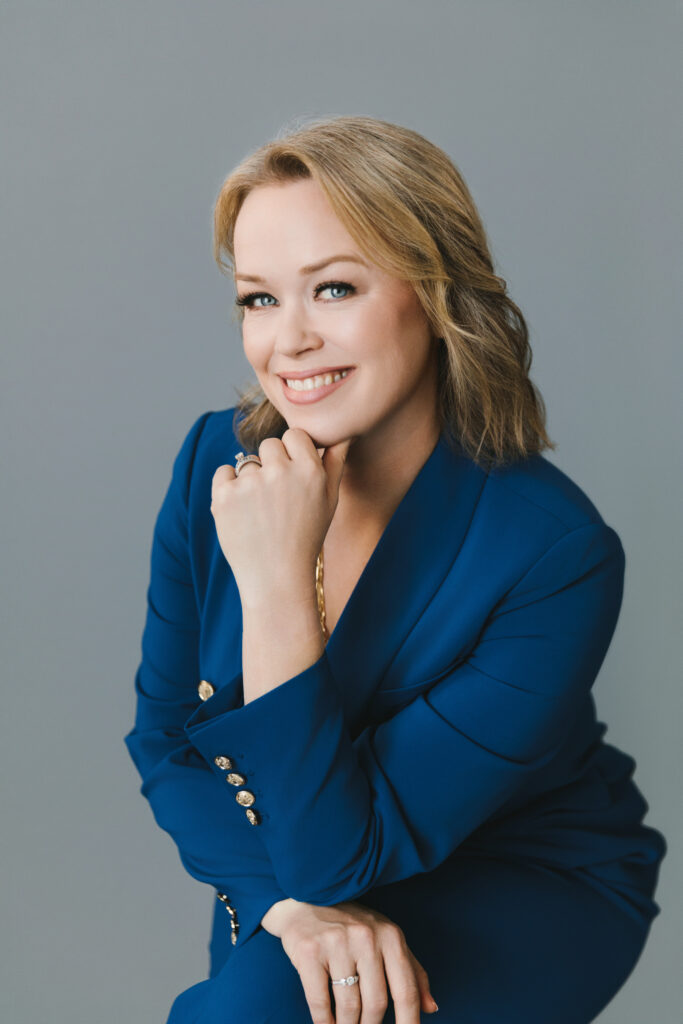 Headshot of a woman wearing a blue blazer with a grey background. Photography by Lindsay Hite
