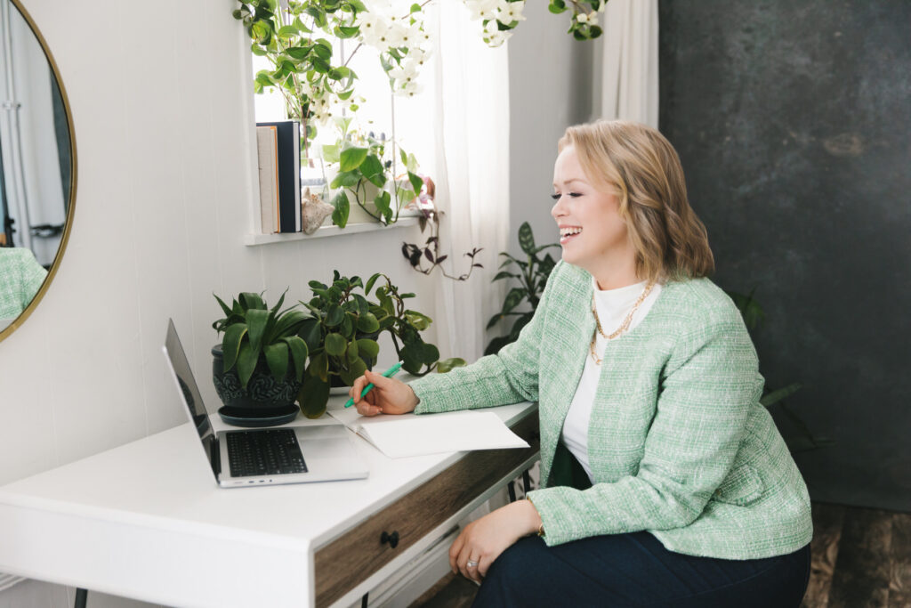 Woman in a green blazer sitting at a desk on a virtual meeting on her laptop. Photography by Lindsay Hite