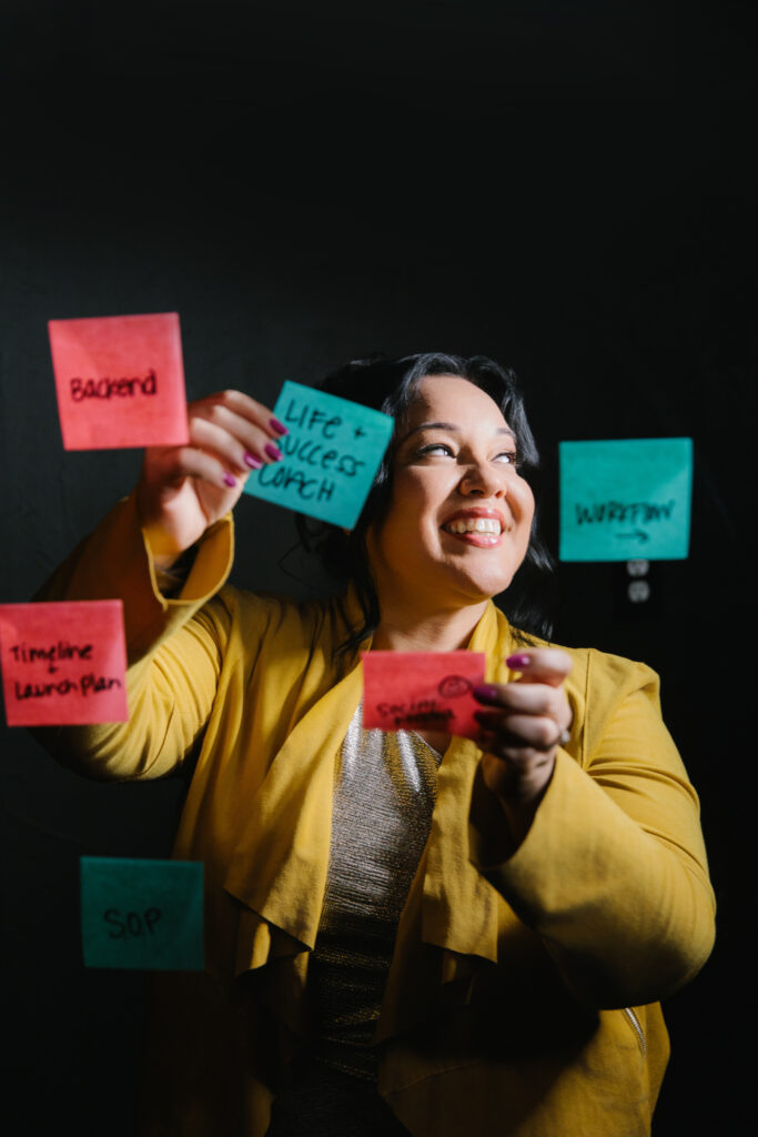 Woman in yellow blazer putting sticky notes on the screen with a black background. Photography by Lindsay Hite