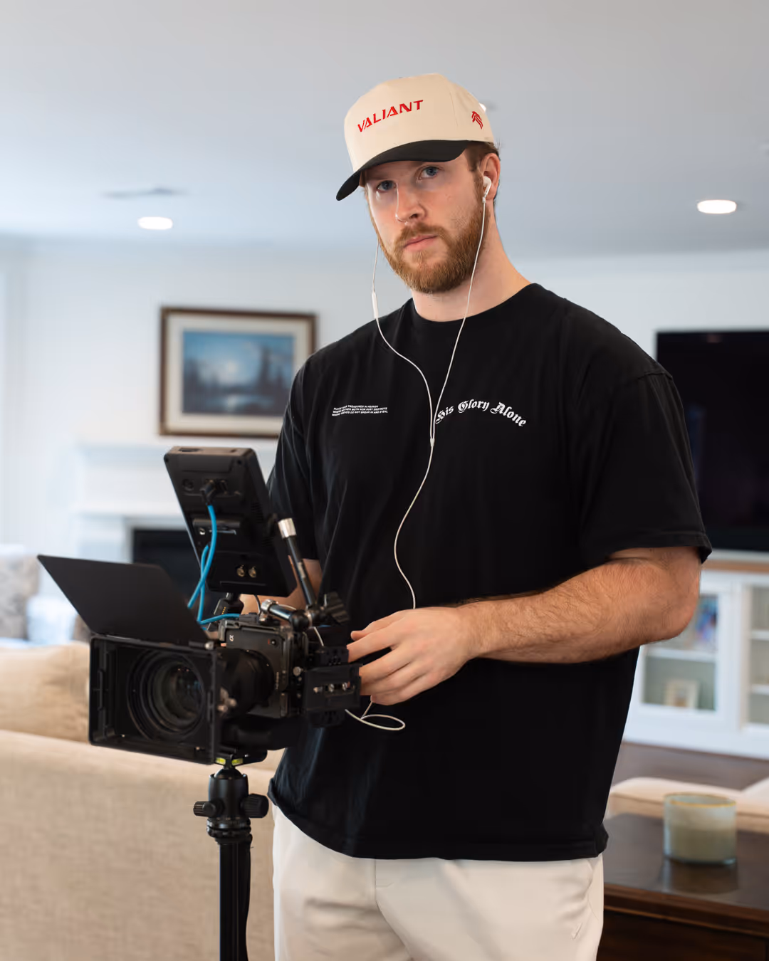 Jared wearing a beige cap and black shirt adjusting a professional video camera indoors.