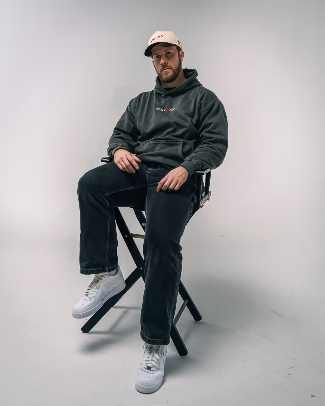 Jared wearing a black hoodie and white cap with the word 'Valiant' sitting on a black director's chair against a plain white background.