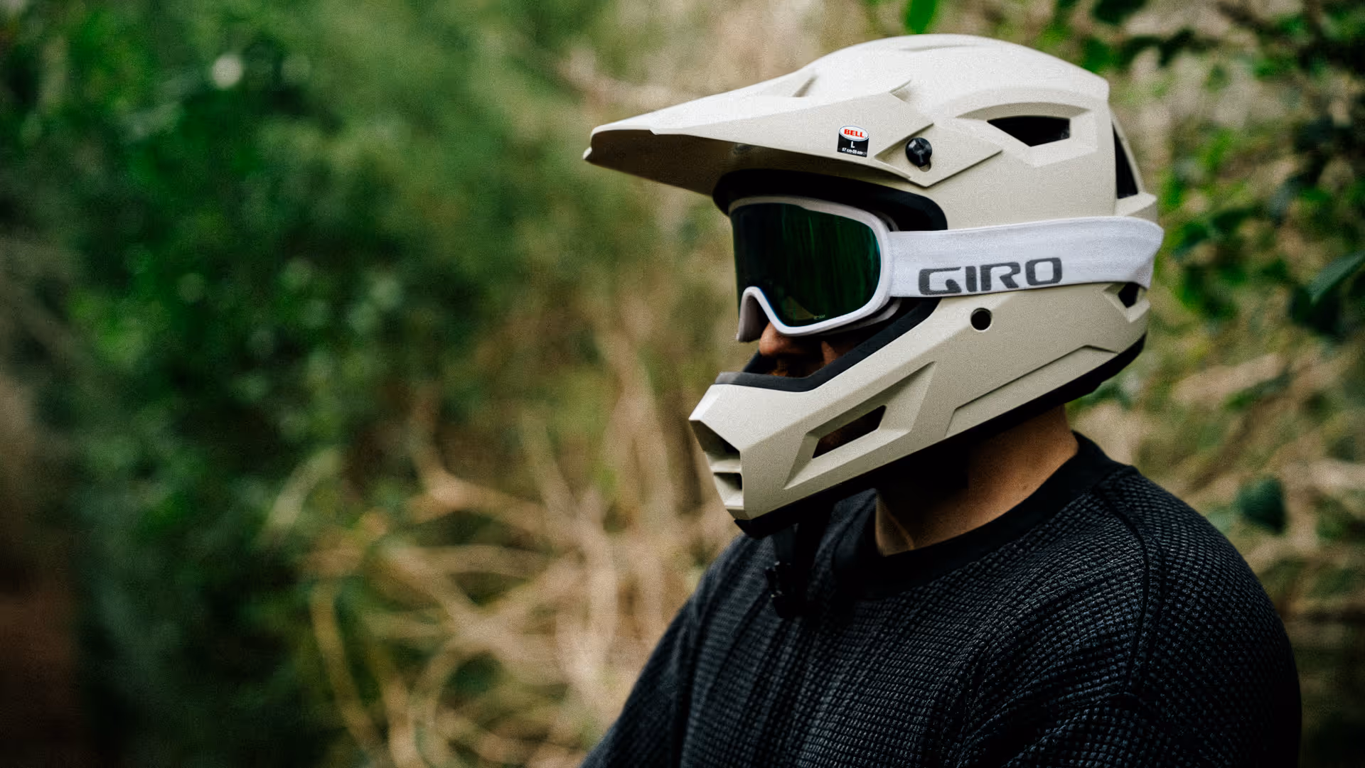 Person wearing a white Bell mountain biking helmet with white Giro goggles against a green outdoor background.