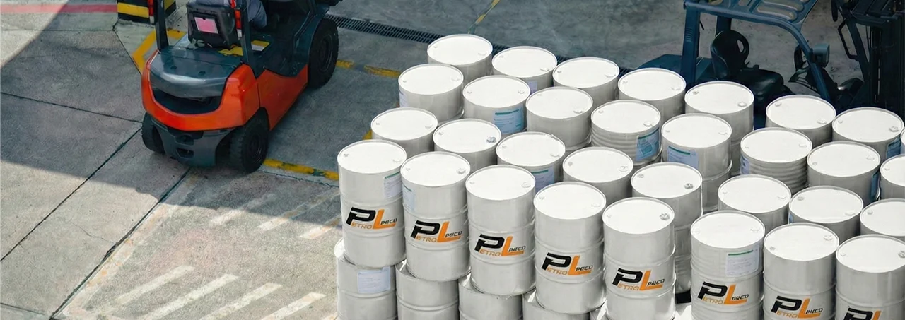 Stacked white barrels labeled 'Petro' organized outdoors near an orange forklift on concrete ground.