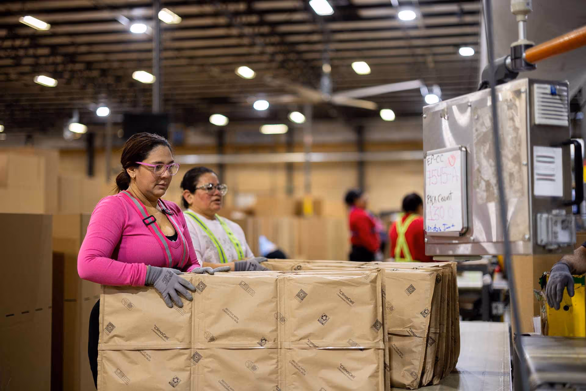 Two women wearing gloves and safety glasses working in a warehouse handling ClimaCell.