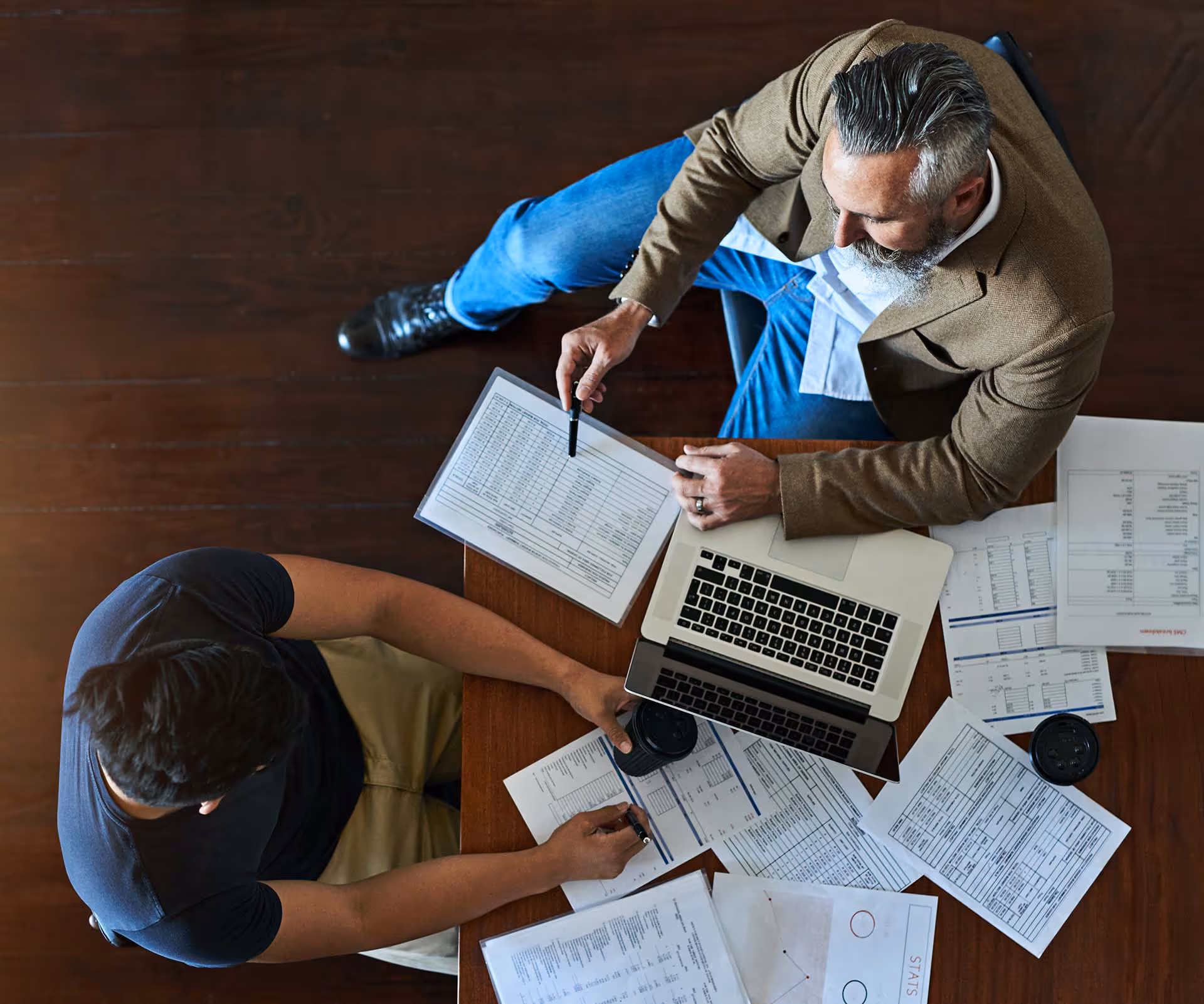 Two men at table working on costs at computer.