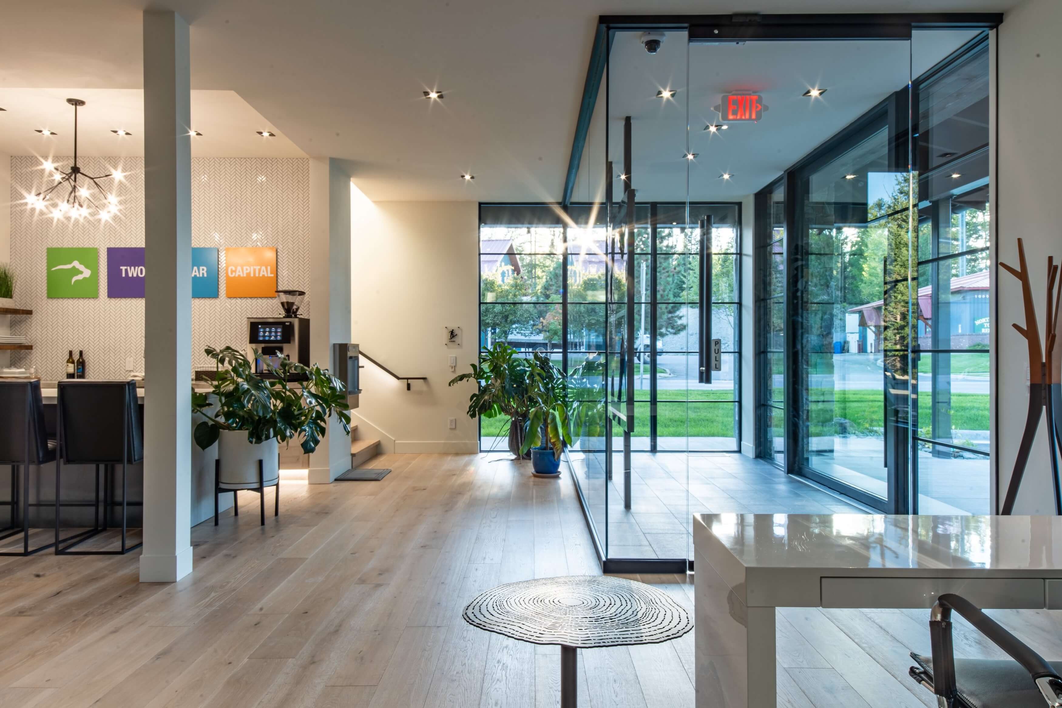 Modern office lobby with glass entrance, wood flooring, plants, and seating area near reception desk.