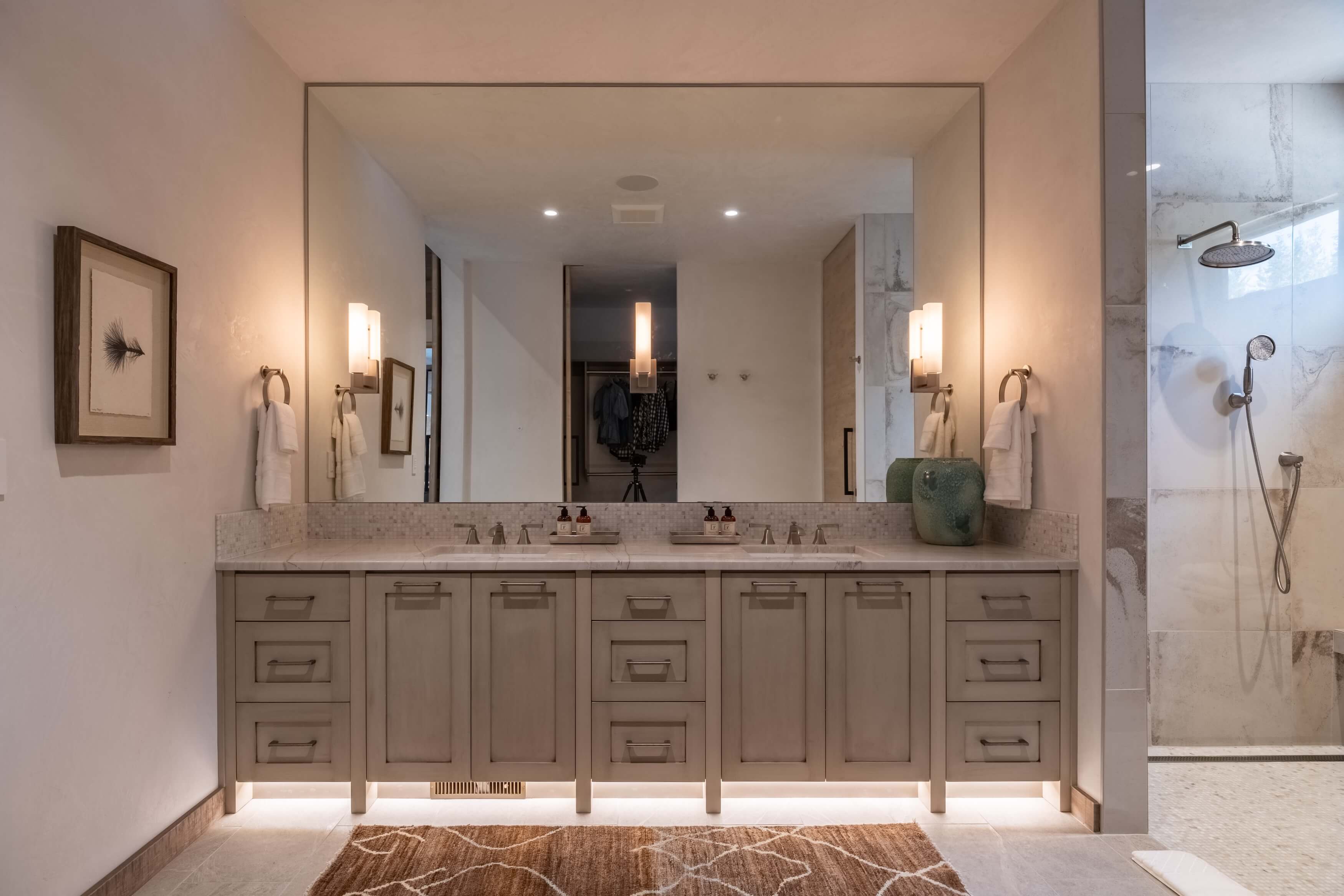 Modern bathroom with double sink vanity, large mirror, towel holders, and glass-enclosed shower on right.