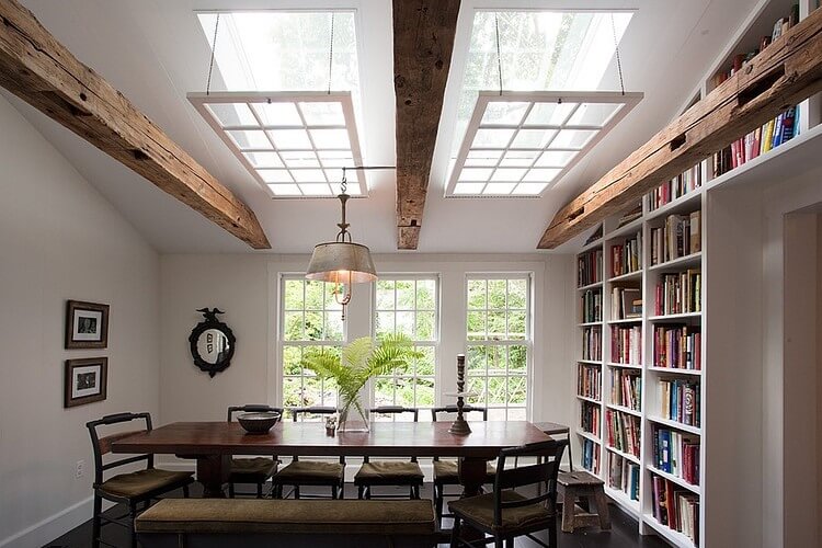 Dining room with wooden table, chairs, built-in bookshelf, exposed beams, and large windows.