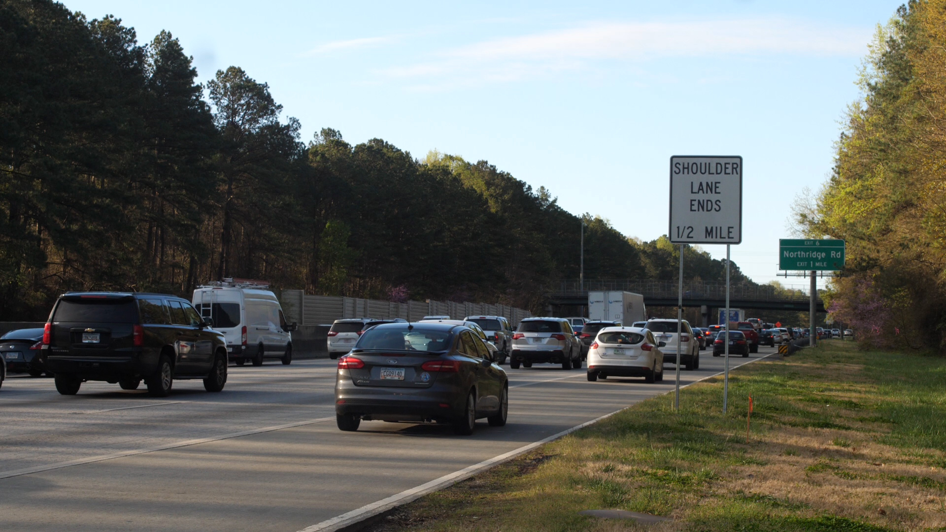 Multiple cars driving on a highway with a sign reading 'Shoulder Lane Ends 1/2 Mile' and another indicating 'Exit 6 Northridge Rd Exit 1 Mile'.