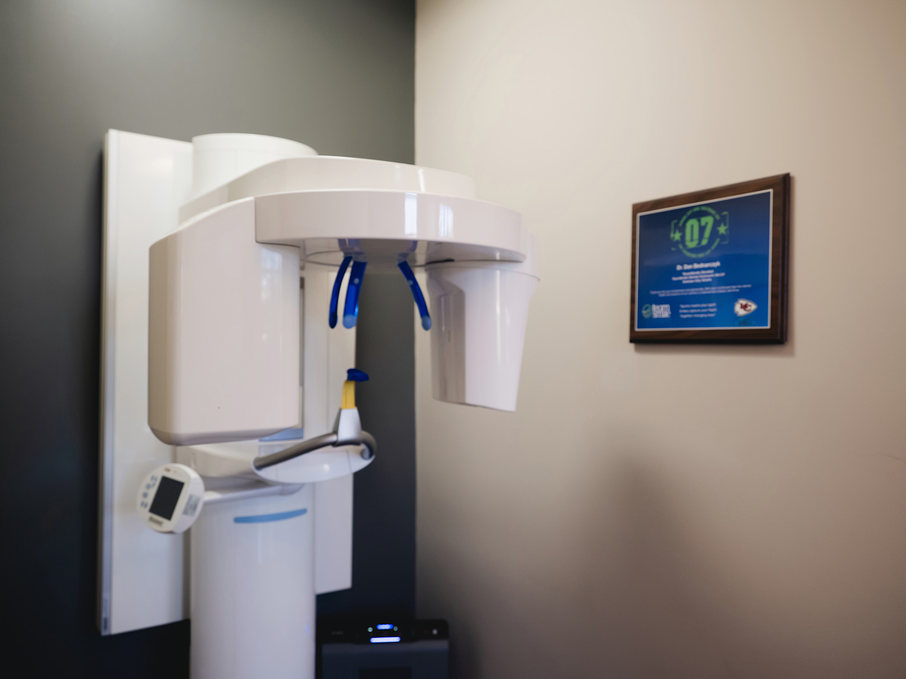 White panoramic dental X-ray machine with blue bite handles in a dental office.