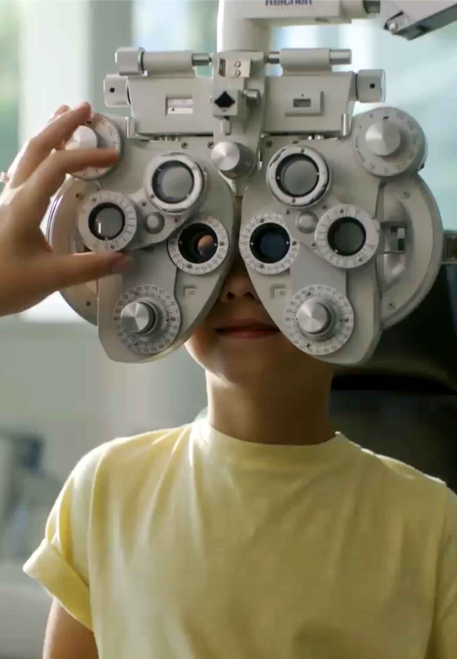 Child wearing yellow shirt undergoing an eye exam using a phoropter.