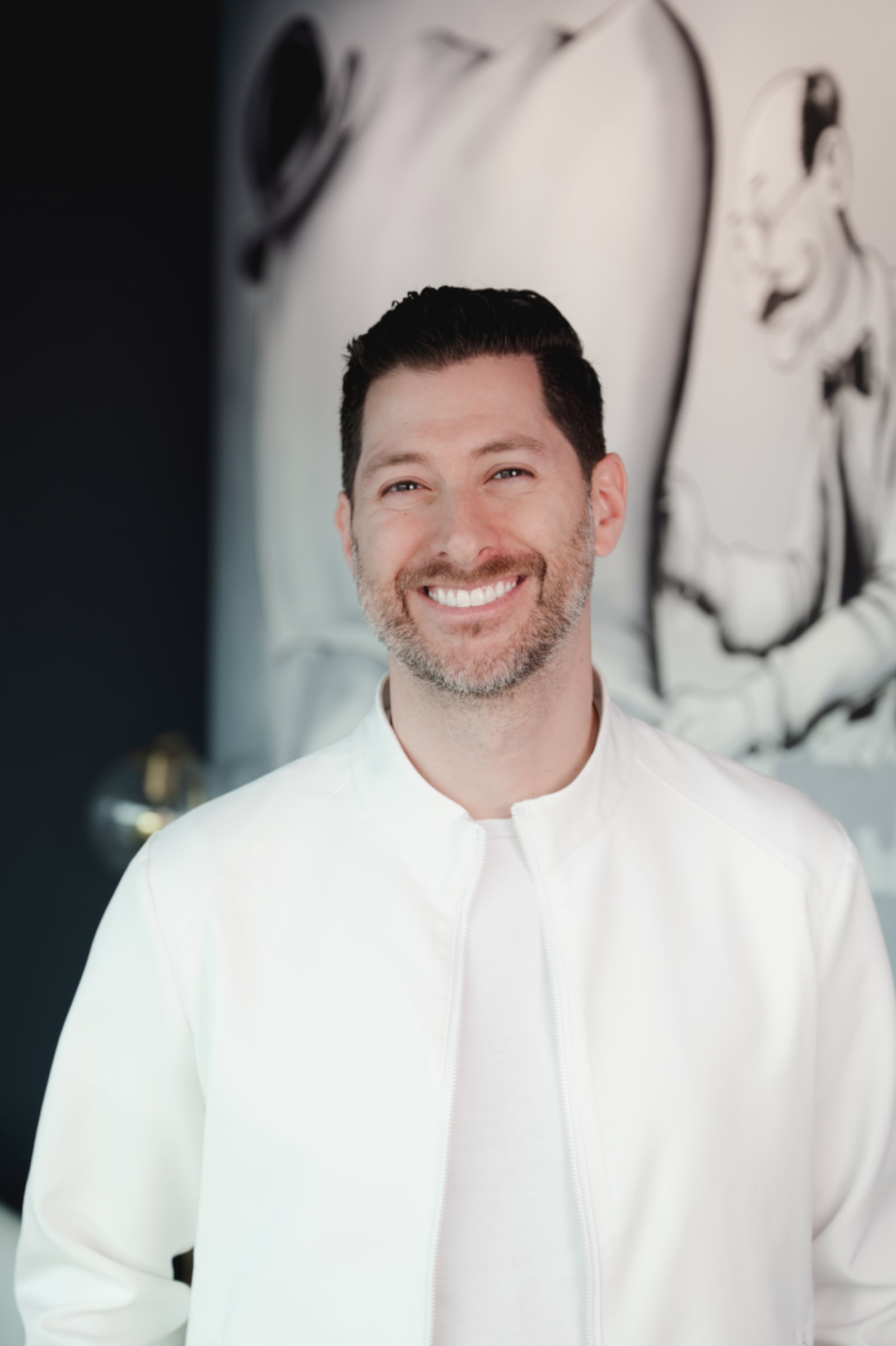 Male dentist in white coat smiling in dental office with treatment room background
