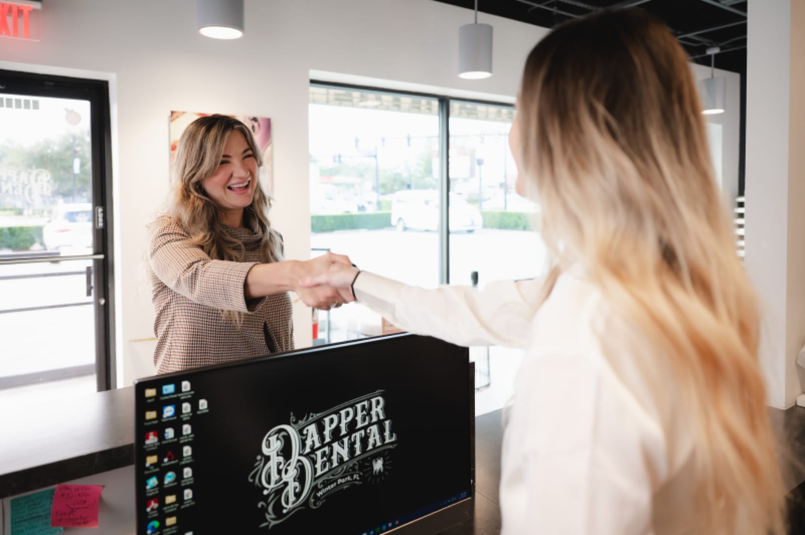 Female receptionist greeting patient at Dapper Dental front desk in modern office setting.