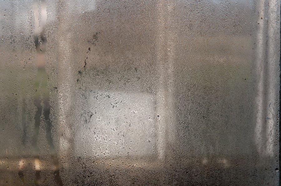 Foggy window covered with condensation droplets on the outside obscuring the view of the outside world.