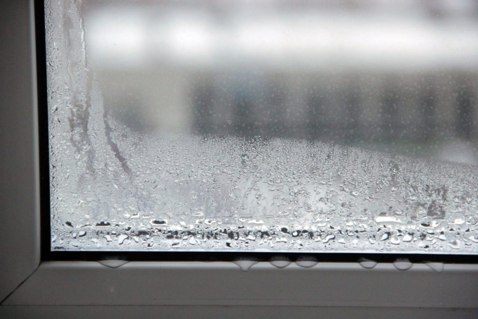 Close-up of a fogged interior window with condensation droplets and water beads on the glass and frame.