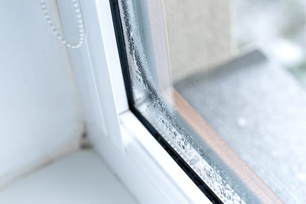 Close-up of condensation and water droplets between the panes of a double-pane window.