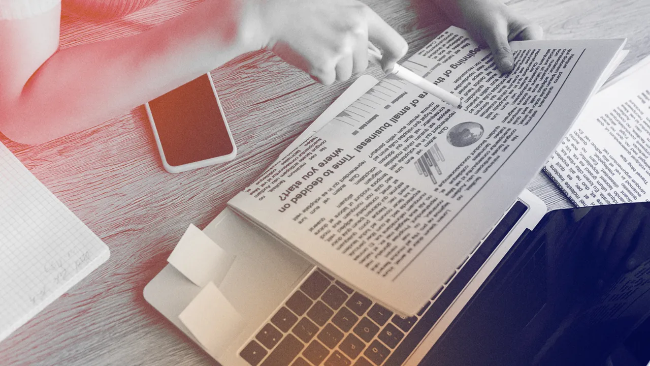 Click2View copywriter editing a printed editorial piece on a desk with a laptop and smartphone nearby