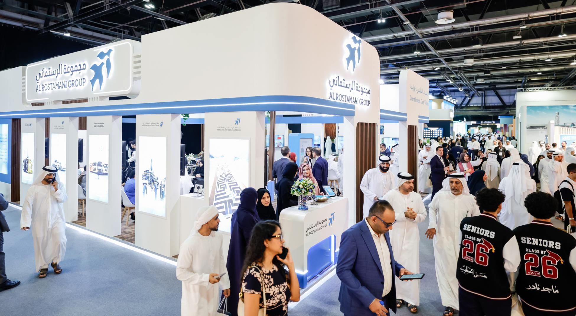 Crowd of attendees at the Al Rostamani Group booth during a busy career fair, with branded display panels and staff engaging visitors.