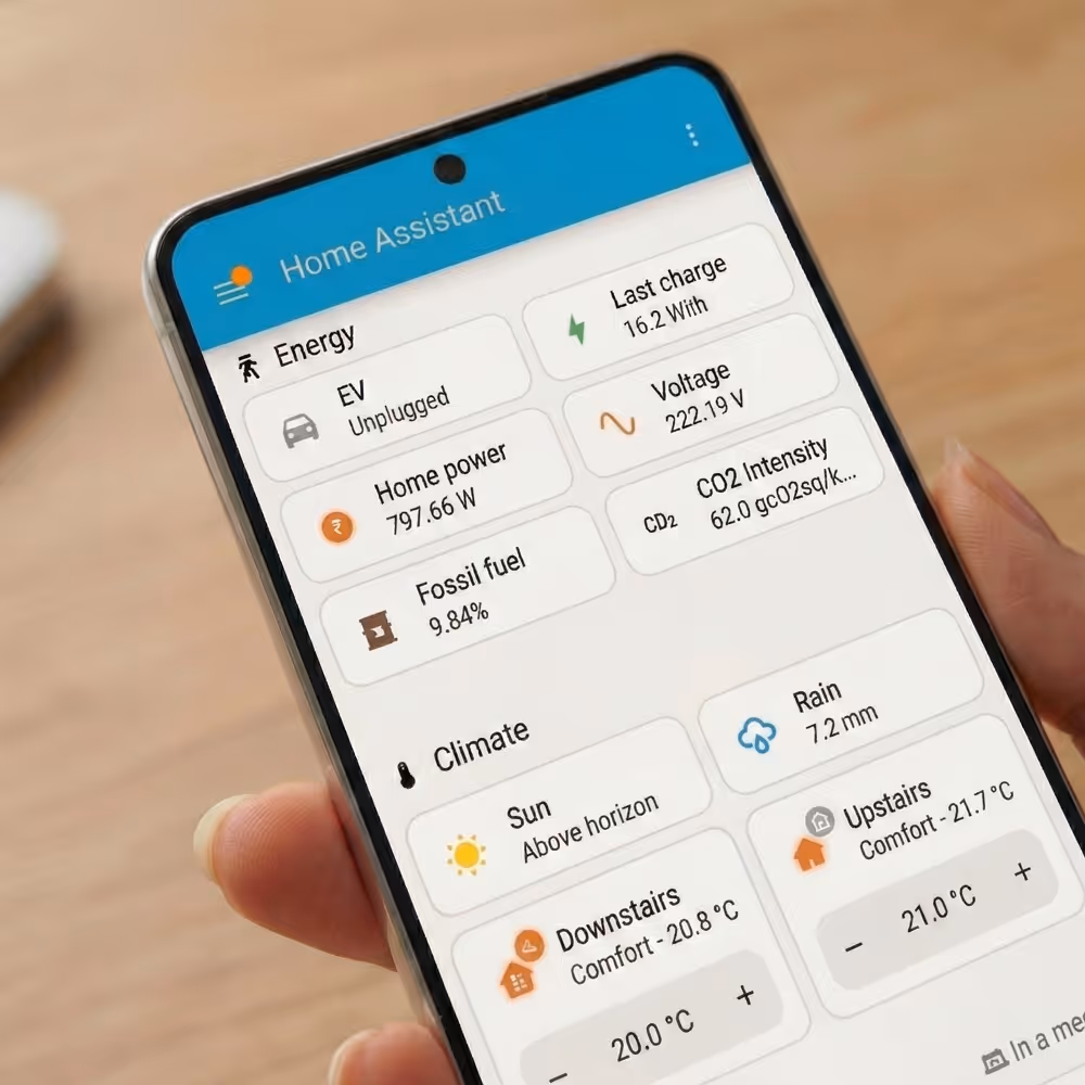 Smartphone displaying a Home Assistant app showing energy stats including EV unplugged, home power usage, fossil fuel percentage, last charge, voltage, CO2 intensity, and climate controls for sun, rain, downstairs and upstairs temperatures.
