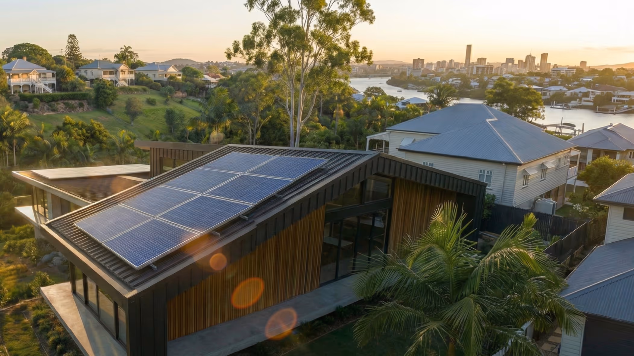 Modern house with solar panels on the roof overlooking a river and city skyline at sunset.