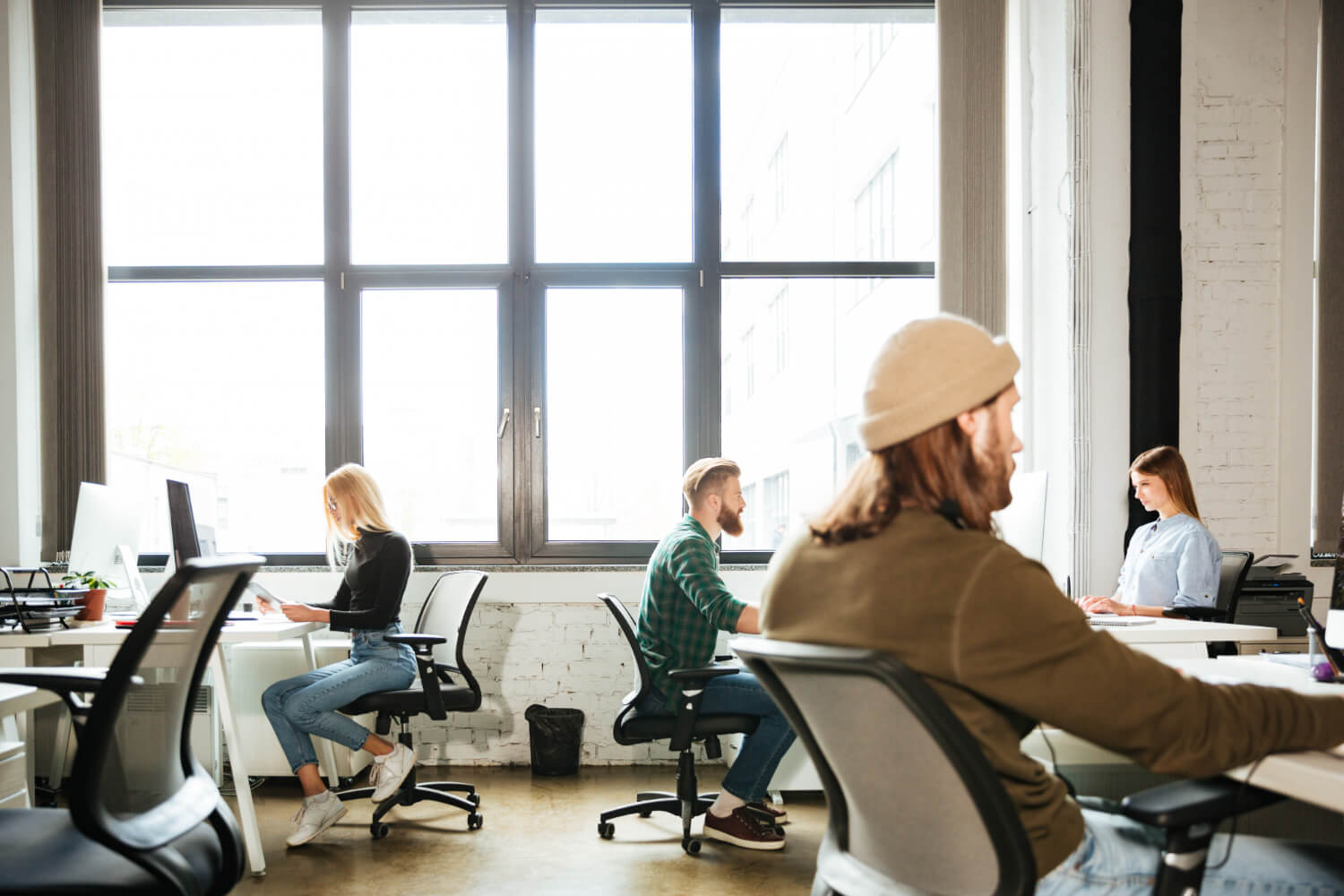 Office workers sitting at desks in an open-plan workspace showing typical desk posture and tension patterns